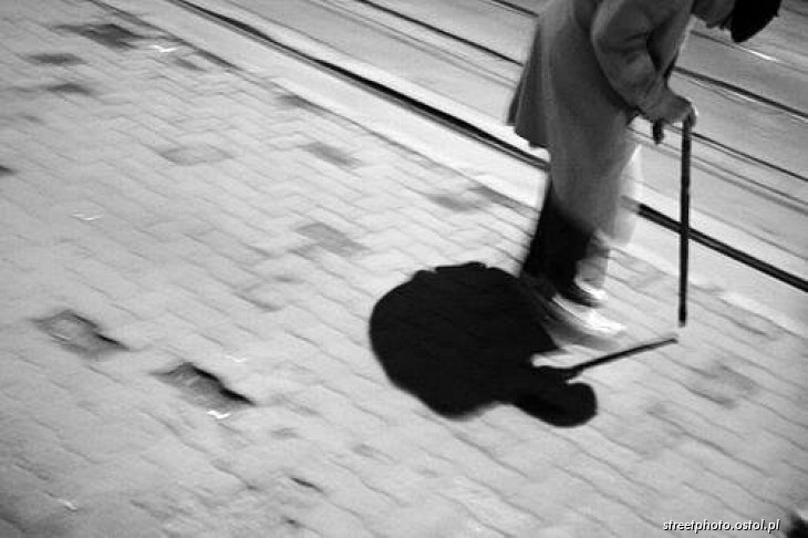Starzec na ulicy. Zgarbiony człowiek o lasce, ludzie w fotografii